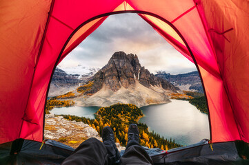 Wall Mural - Hiker man relaxing in a tent with mount assiniboine view in autumn forest