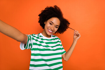 Sticker - Self-portrait of attractive cheerful wavy-haired girl touching curls isolated over vivid orange color background