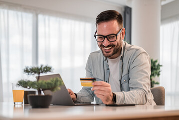 Wall Mural - Smiling businessman making online payment with credit card from laptop at desk