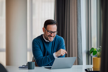 Wall Mural - cheerful business professional working on laptop at desk in corporate office