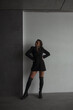 © NASTYA PALEHINA - teen fashion leisure. young girl in black dress-jacket and over the knee boots stands casual and looks apart with cute smile near white and gray studio wall background. lifestyle concept, free space