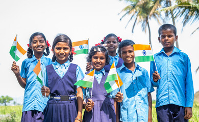 group of happy smiling village school kids in unifrom holding Infian flag by looking at camera during independence day celebrations - conept of patriotismsm, diversity and real people.