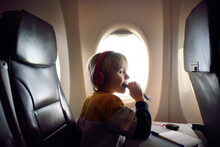 Cute Little Boy Traveling By An Airplane. Child Using Player To Listen Music Or Audiobook During Flight And Eating Cereal Bar. Entertainment For Kids On A Board Of Plane