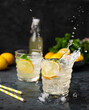 © Kufotos - Two glasses of Lemonade drink with fresh lemon and splashes. Refreshing cocktails with lemons, mint and ice on dark background. Summer cold drinks concept
