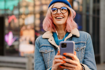 Young white woman in earphones laughing and using cellphone