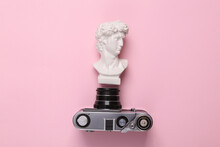 Retro Camera With David Bust On Pink Pastel Background. Top View