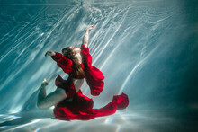 Attractive Red-haired Young Woman Swims Beautifully Underwater In A Red Dress
