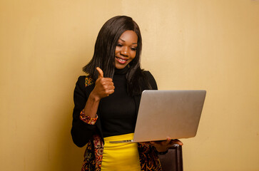 Wall Mural - close up of a beautiful lady smiling as she holds a laptop on her hand and did thumbs up