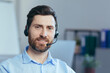 © Liubomir - Close-up portrait of a businessman with a headset for a video call, a man looking at the camera smiling, a call center operator