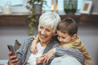 © Dragana Gordic - Grandma and grandson spend time together watching a funny video or cartoon on the phone, laughing while grandson hugs her. They enjoy their modern home.