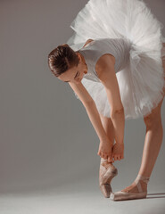 classic ballet posing. young slim dancer, brunette girl ballerina is tying ribbons on pointe shoes i
