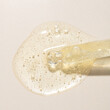 Top view of transparent pipette dropper with light golden drop of serum cosmetics, oil, gel ou cream on beige  background and bubbles of air. Minimal beauty concept, macro closeup with copy space