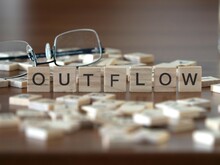 Outflow Word Or Concept Represented By Wooden Letter Tiles On A Wooden Table With Glasses And A Book