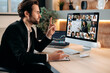 © Kateryna - Distant video briefing. Successful business man, sit in office in front of computer, conducts a financial brainstorm with business multiracial partners, discussing financial strategy, analyzing risks