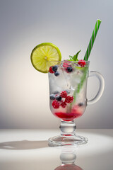 Wall Mural - Refreshing summer cocktail with ice, lime and berries in a glass with a straw, vertical image