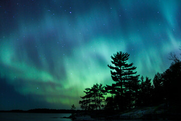 northern lights erupt over a lake in minnesota in a dark sky overhead shining rainbow of aurora ligh