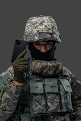 Wall Mural - Portrait of miltray man dressed in camouflage uniform holding cellphone like handgun. Information warfare.