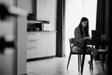 Young Female Freelancer Dressed In Home Clothes Working On Laptop Sitting At The Table In The Kitchen. Stylish Girl On Workplace At The Desk. Distance Learning Online Education