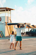 © _KUBE_ - Summer family activity. Father and daughter are walking along the beach. Man holding a sup board. Back view. Sunset light. Vertical