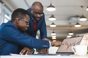 Wall Mural - Two African American business partners are working on a laptop studying stock market charts and technical analysis. Training in investment and analysis of macroeconomic and financial indicators