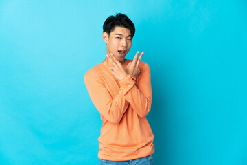 Wall Mural - Young Chinese man isolated on blue background smiling and showing victory sign