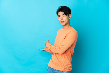 Wall Mural - Young Chinese man isolated on blue background extending hands to the side for inviting to come