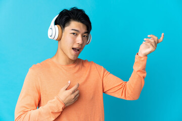 Poster - Young Chinese man isolated on blue background listening music and doing guitar gesture