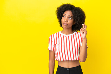 Wall Mural - Young African American woman isolated on yellow background with fingers crossing and wishing the best