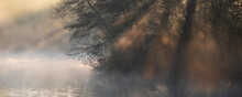 Beautiful Landscape Image Of Sunrise Mist On Urban Lake With Sun Beams Streaming Through Tress Lighting Up Water Surface