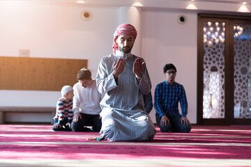 Prayer with a thankful heart. Group of muliethnic religious muslim young people praying together inside beautiful modern mosque