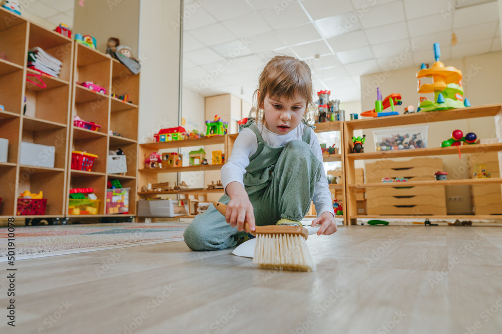 Little girl sweeping the floor using a dustpan and a broom at ...