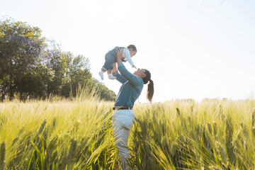 single mom plays with her son in a wheat field at sunset