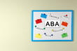 Board with abbreviation ABA and different colors on beige wall, space for text