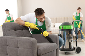 Poster - Professional janitor in uniform vacuuming armchair indoors