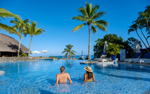 Beautiful Tropical Beachfront Hotel Resort With A Swimming Pool, Sun-loungers, And Palm Trees , A Paradise Destination For Vacations. Couple Men And Woman Mid Age On A Luxury Vacation