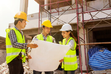 Team engineers led by female architect foreman explains construction design to the two male workers and divides the construction work on site renovate building according project according plan.