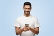 Attractive man in t-shirt looks attentively at cellphone browsing web pages and smiling