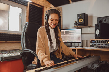 Stylish woman musician, sound composer playing synthesizer and rehearsing new song in the modern recording music studio