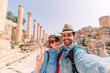 a young couple with hat taking a selfie while enjoying the beautiful landscape of the ancient ruins of Jerash in a sunny day