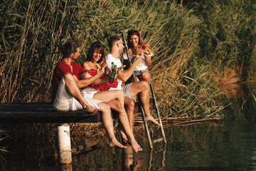 Wall Mural - Happy group of young people drinking beer on a dock by the river during the summer sunny day