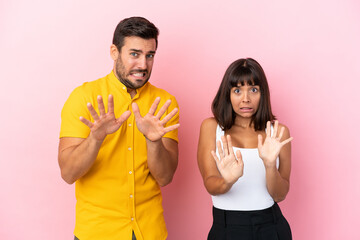 Wall Mural - Young couple isolated on pink background is a little bit nervous and scared stretching hands to the front