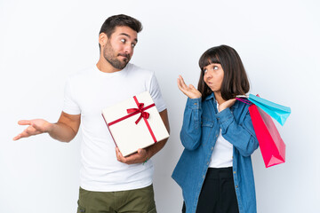 Wall Mural - Young couple holding shopping bags and present isolated on white background making unimportant gesture while lifting the shoulders