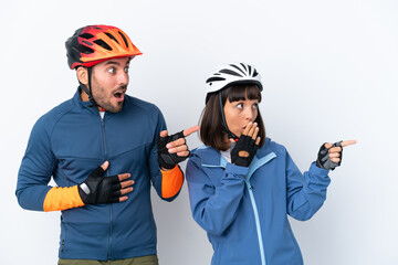 Wall Mural - Young cyclist couple isolated on white background pointing finger to the side with a surprised face