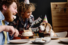 Happy Young Couple Congratulating Their Adorable Dog With Birthday Cake While Sitting At Table