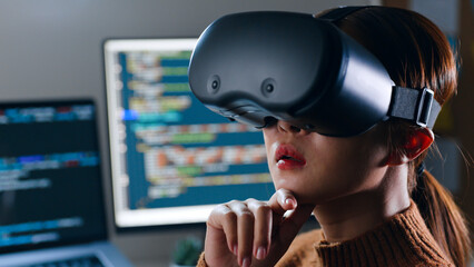 Wall Mural - Young Asian woman, developer programmer, software engineer, IT support, wearing virtual reality headset developing and programming VR game application at night overtime.