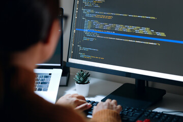 Young Asian woman, developer programmer, software engineer, IT support, wearing glasses working hard at night overtime on computer to check coding in bugging system. Back view