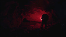Young Man With A Burning Red Signal Flare In His Hand Coming To The Narrow Hole In The Dark Underground Cave. Stock Footage. Tourist Exploring Mysterious Tunnel.
