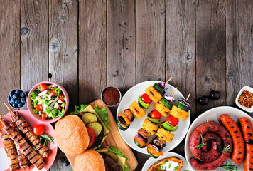 Wall Mural - Summer BBQ or picnic food bottom border. Collection of burgers, grilled meat, vegetables, fruits, salad and potatoes. Top down view on a dark wood background. Copy space.