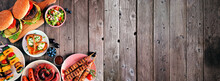 Summer BBQ Or Picnic Food Corner Border. Variety Of Burgers, Grilled Meat, Vegetables, Fruits, Salad And Potatoes. Top View On A Dark Wood Banner Background. Copy Space.