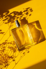 Transparent Bottle Of Perfume On A Yellow Background. Fragrance Presentation With Daylight. Trending Concept In Natural Materials With Beautiful Shadow. Women's Essence.